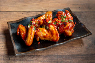 A black plate topped with wings covered in sauce