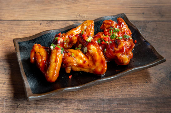 A black plate topped with wings covered in sauce