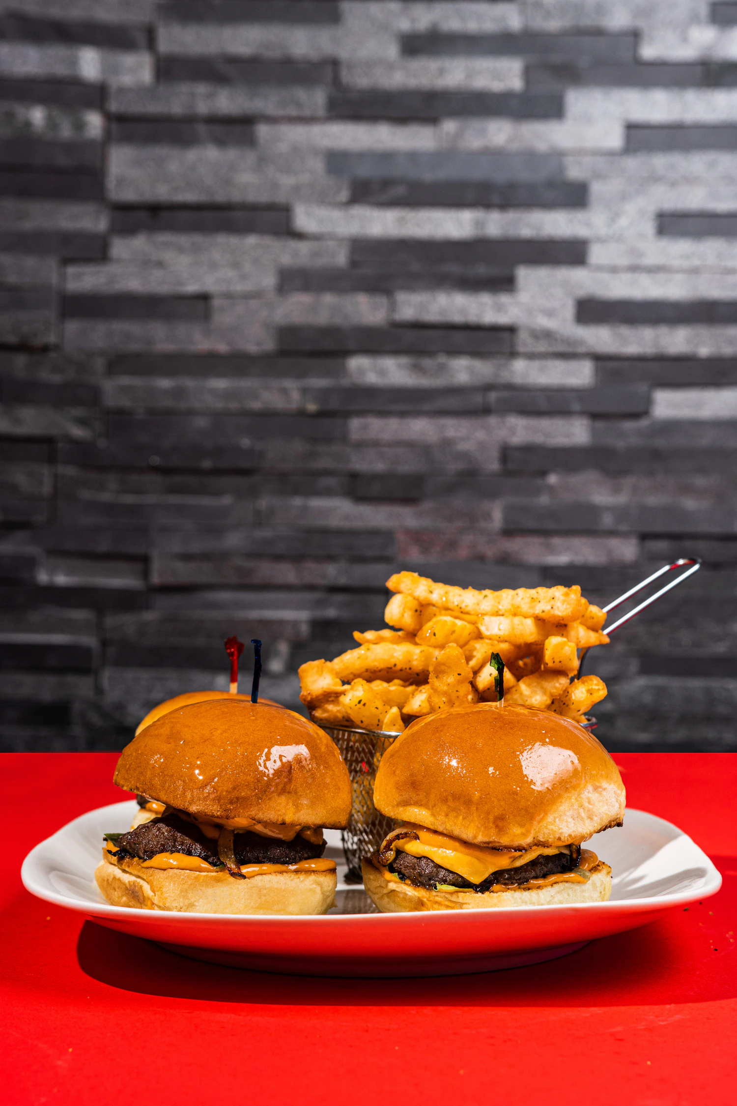 A plate of sliders and waffle fries on a red surface