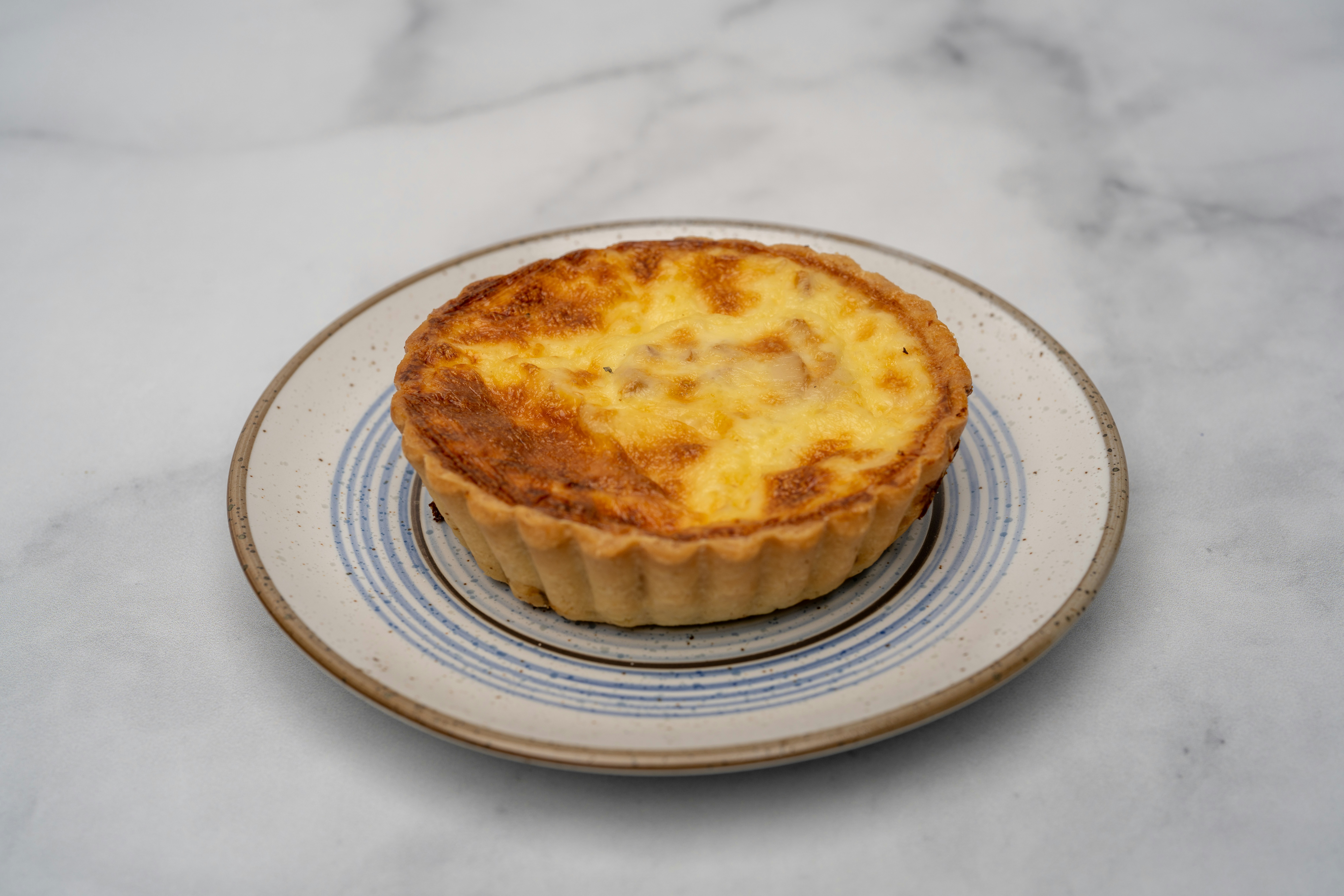 A small quiche on a plate on a marble table