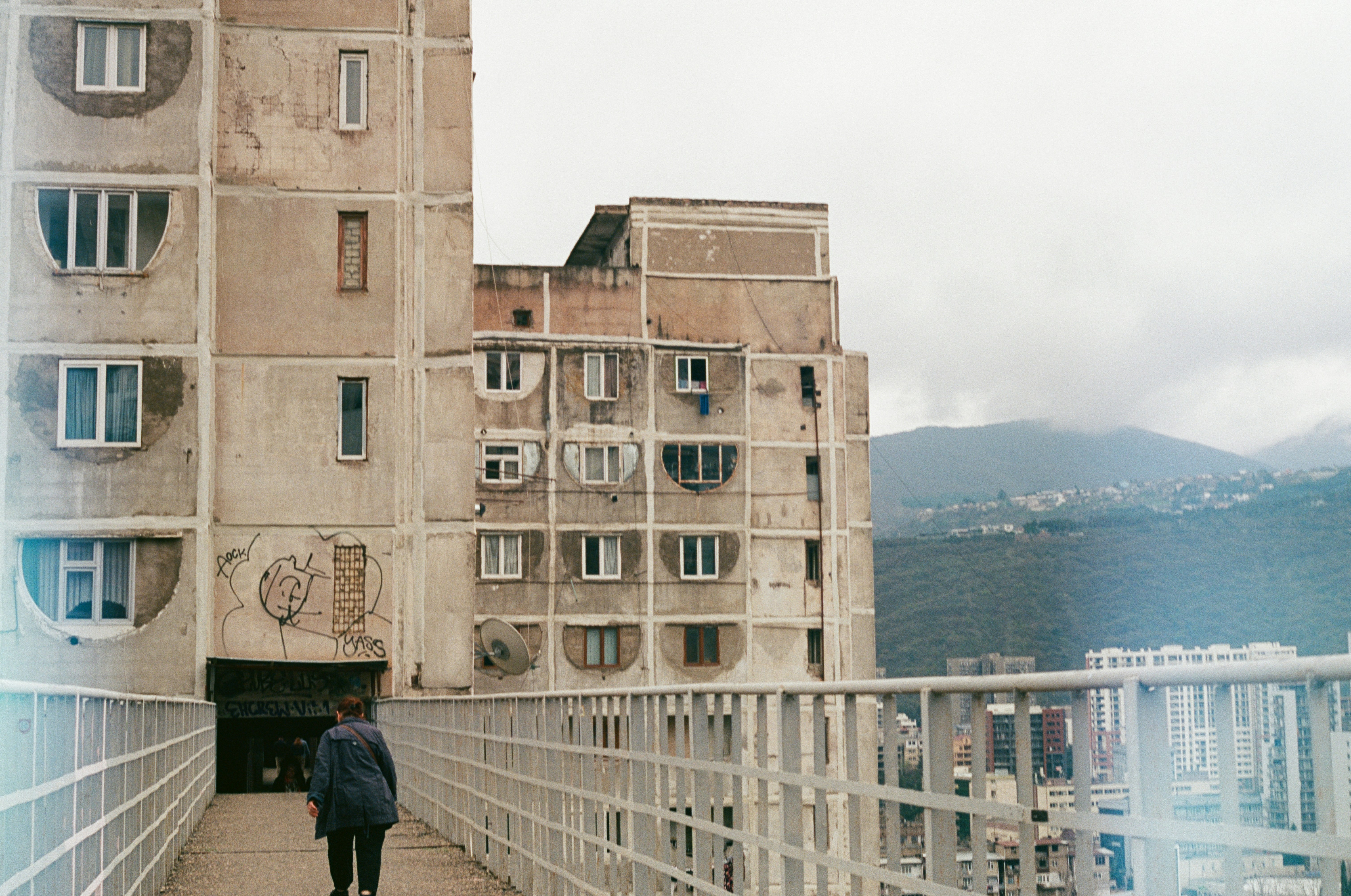 A man walking across a bridge in front of a tall building