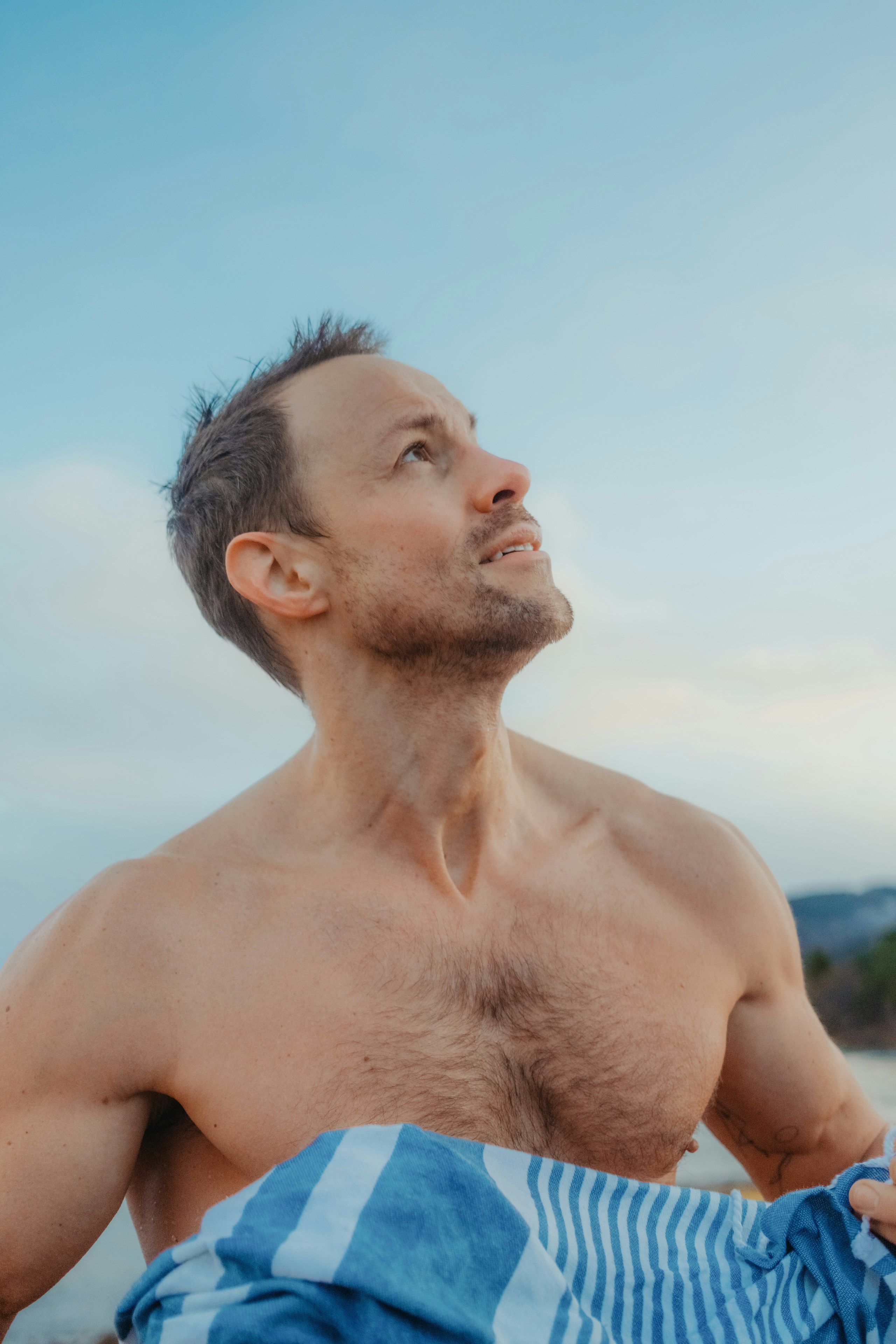 A shirtless man holding a towel on the beach