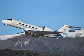 A white and blue plane flying over a mountain
