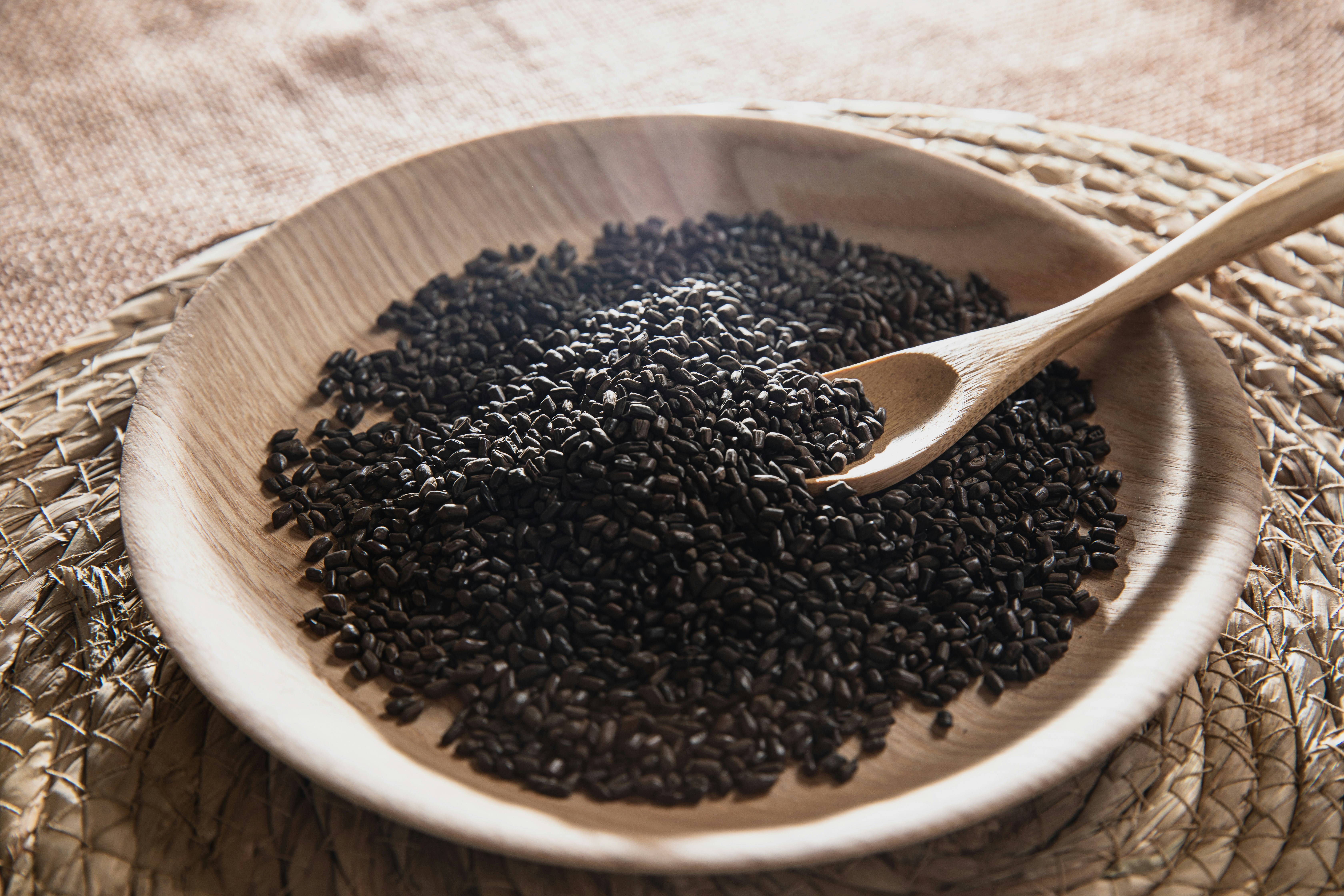 A wooden bowl filled with black seed on top of a table