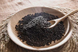 A wooden bowl filled with black seed on top of a table