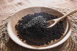 A wooden bowl filled with black seed on top of a table