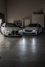 Two white cars parked in a garage next to each other