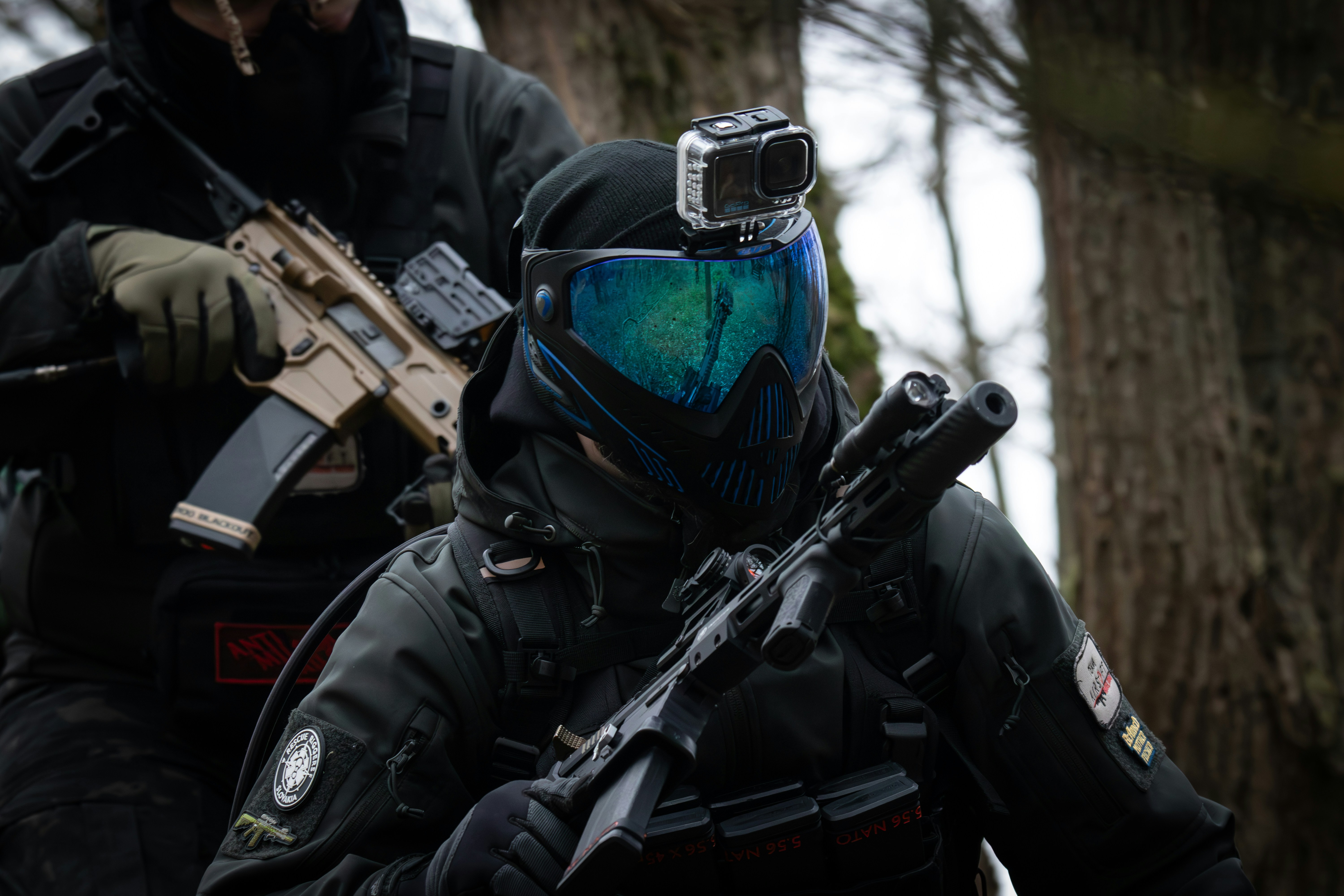 Um homem em uma jaqueta preta e um homem em um capacete azul com uma arma