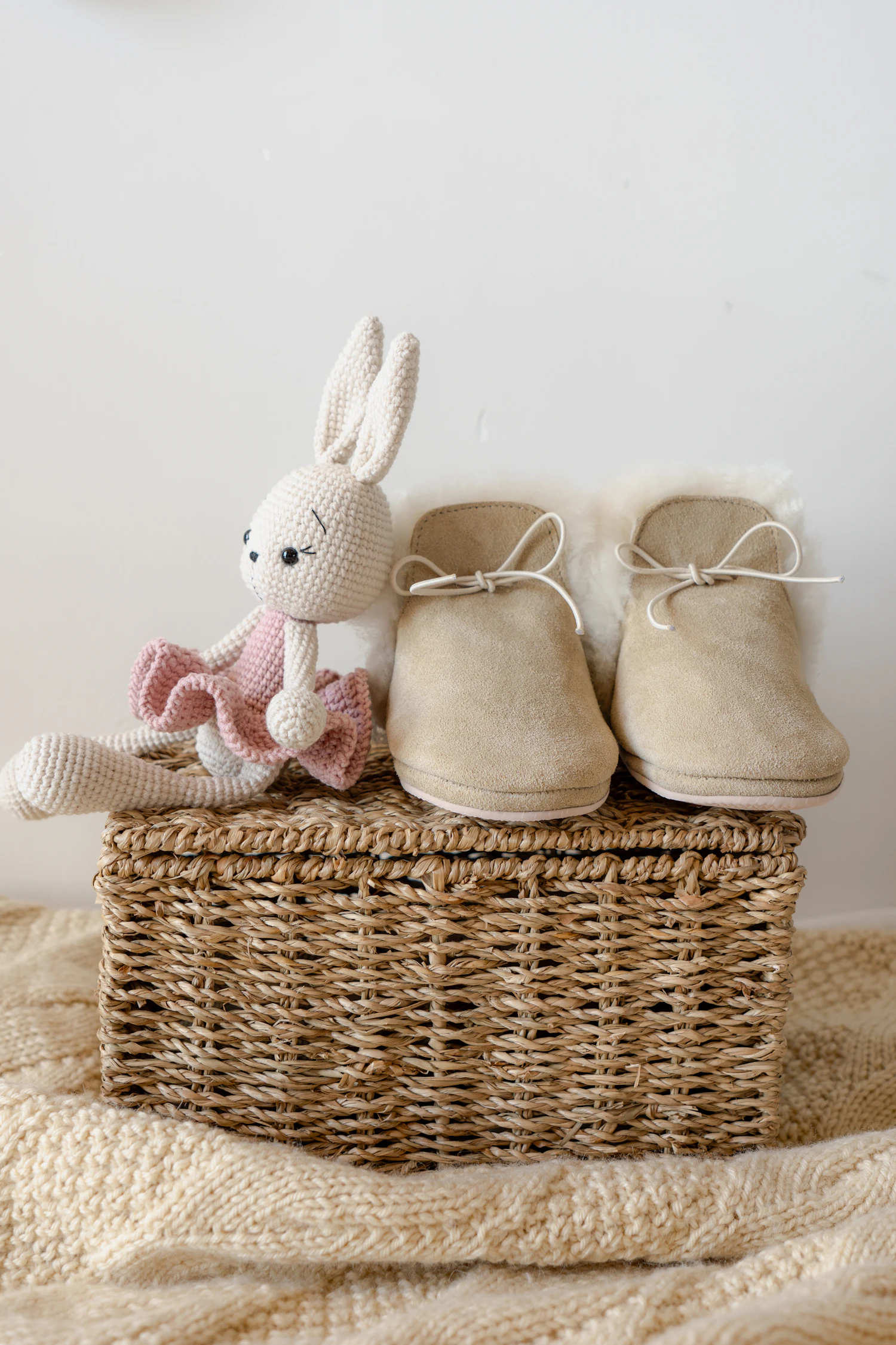 A pair of Bitte first shoes standing on a basket beside a crocheted rabbit