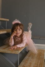 A little girl sitting on a wooden bench wearing a tiara