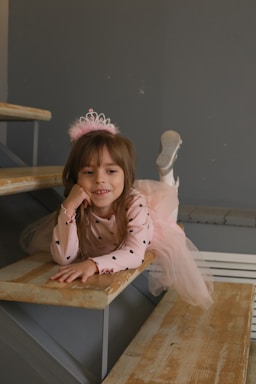 A little girl sitting on a wooden bench wearing a tiara