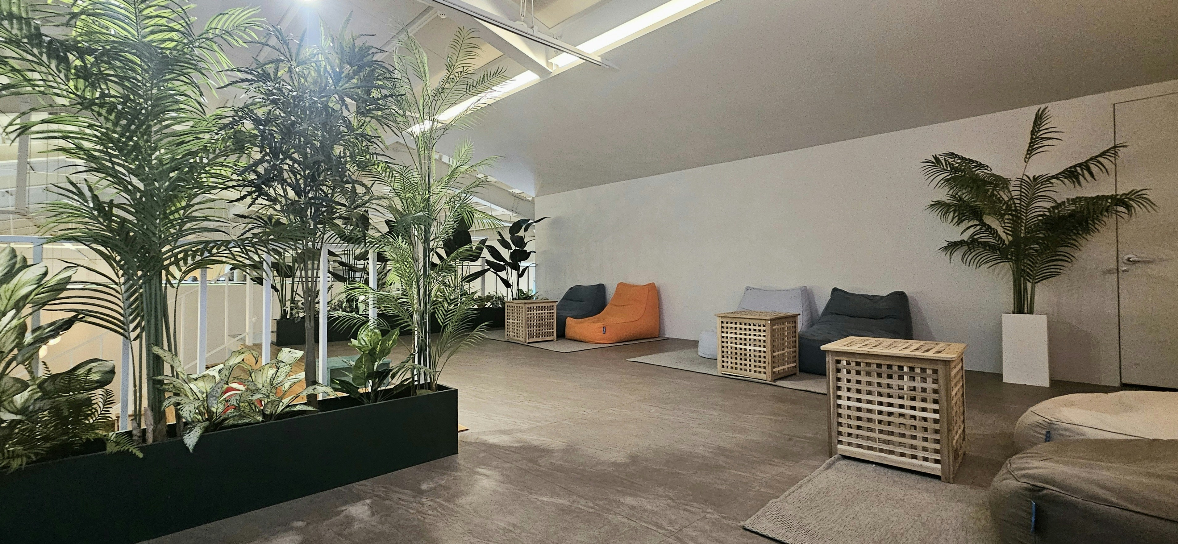 Comfortable lounge area with modular sofas, low tables, warm pendant lights, and green plant installations
