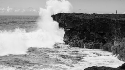 A black and white photo of a wave crashing into a cliff