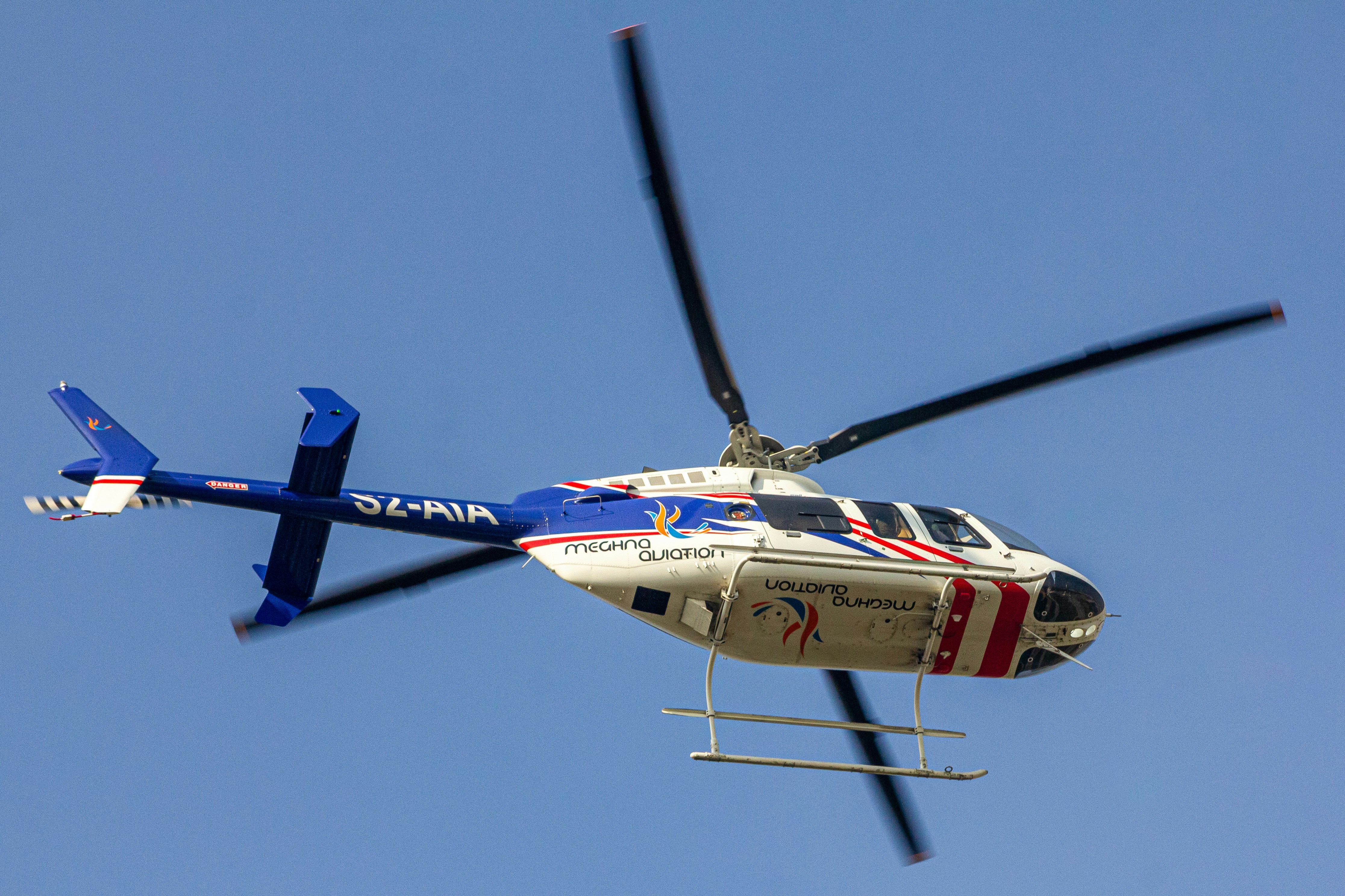 A blue and white helicopter flying through a blue sky