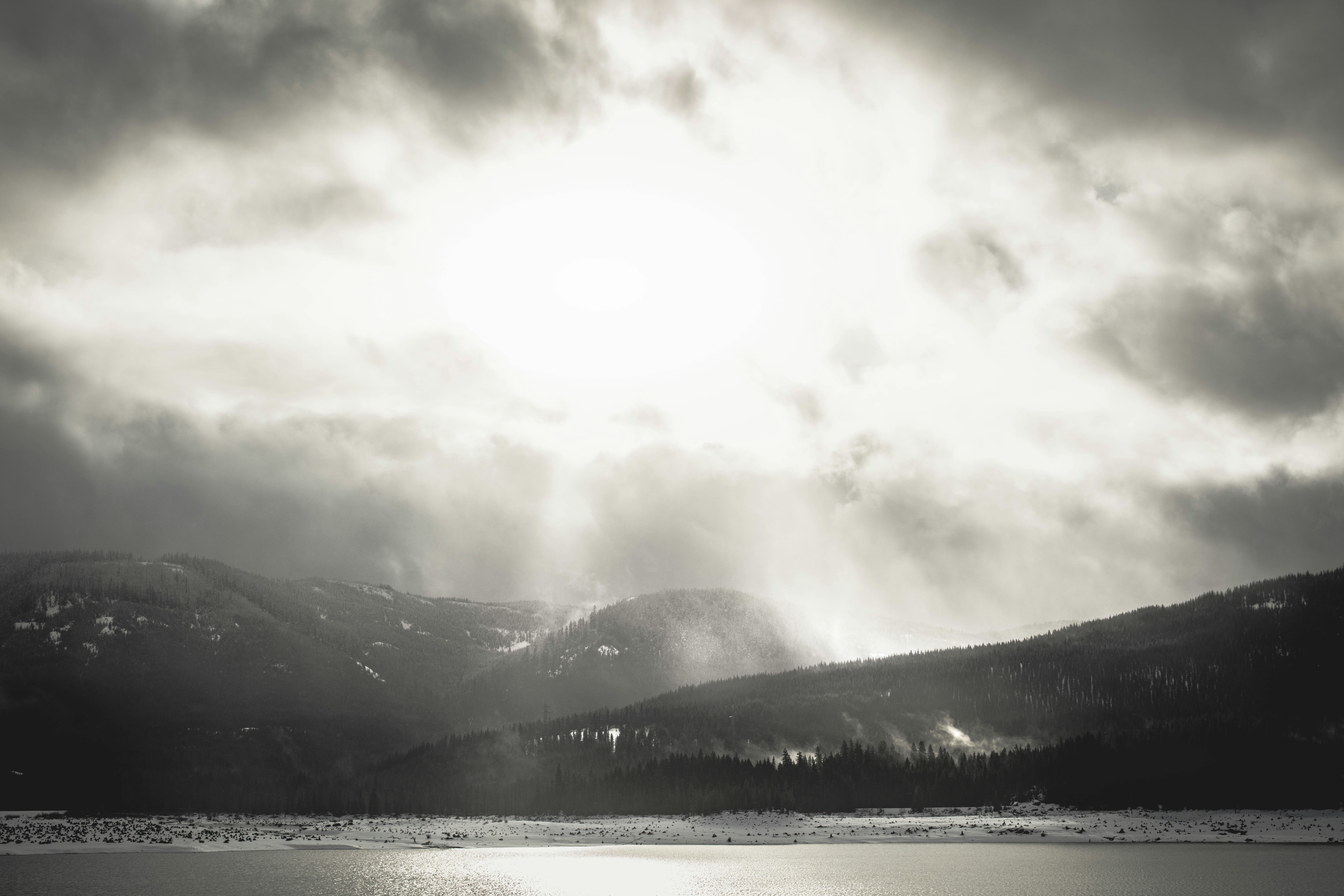 A black and white photo of the sun shining through the clouds