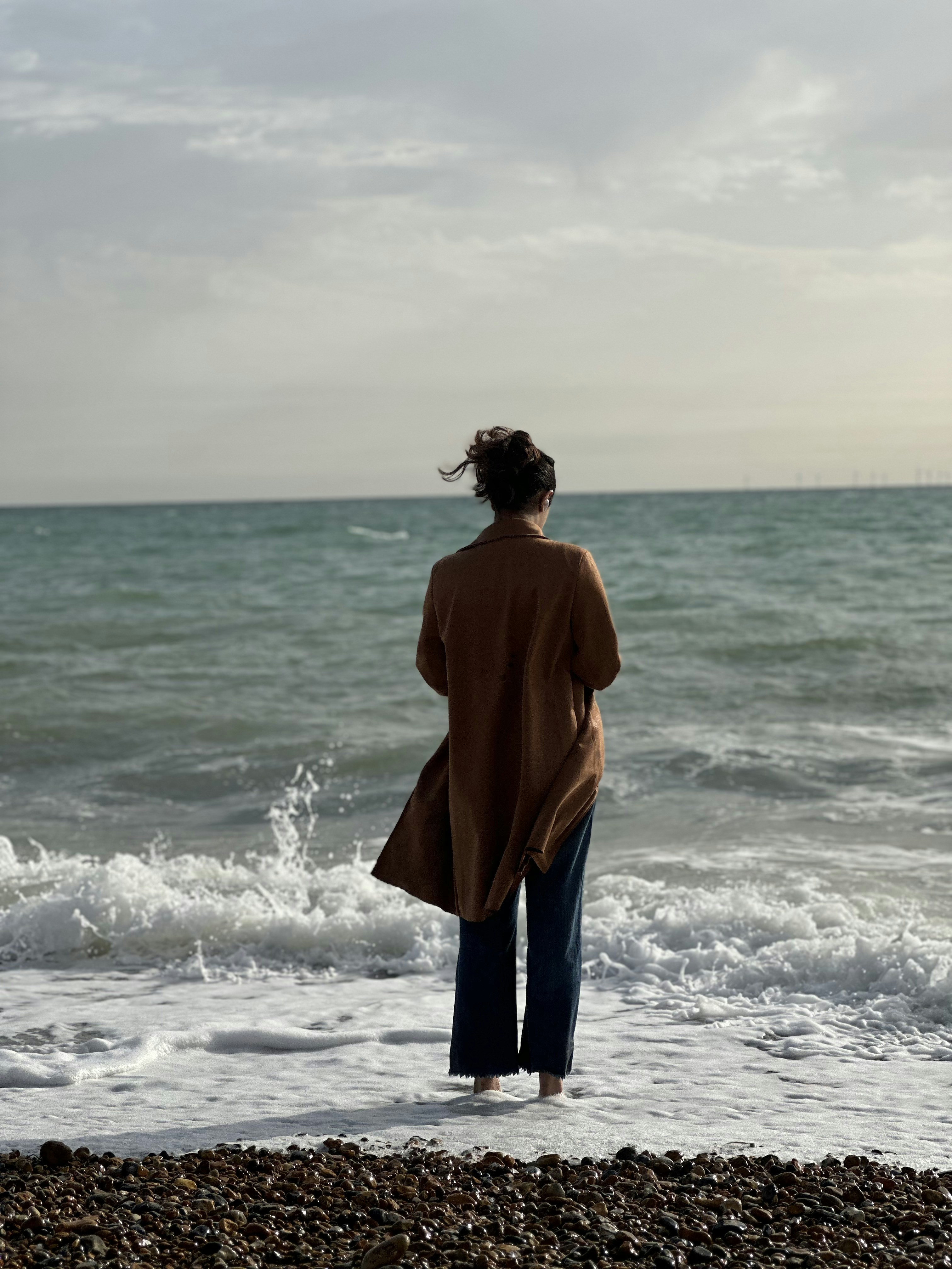 A woman standing on a beach looking out at the ocean