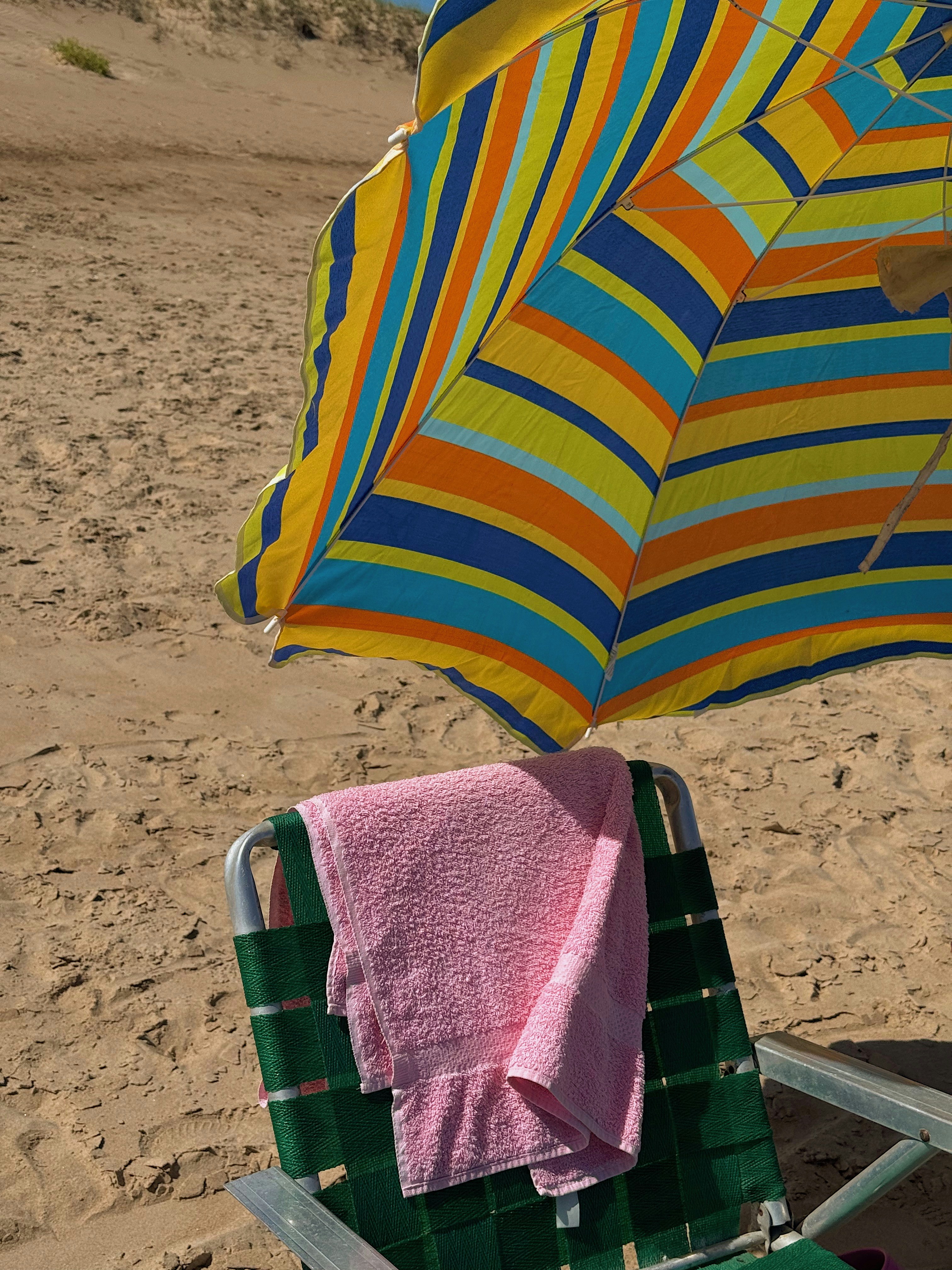 A beach chair with a towel and umbrella on the beach