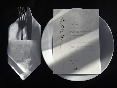 A white plate topped with a piece of paper next to a fork and knife