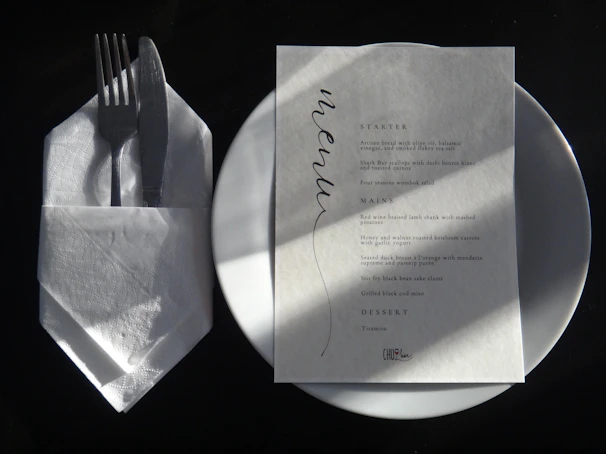 A white plate topped with a piece of paper next to a fork and knife