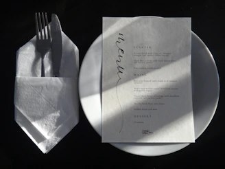 A white plate topped with a piece of paper next to a fork and knife