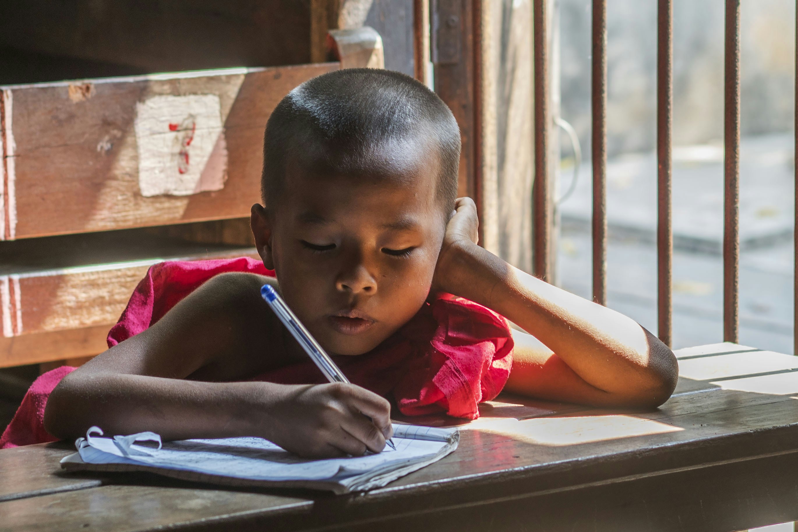A young boy sitting at a table writing on a piece of paper