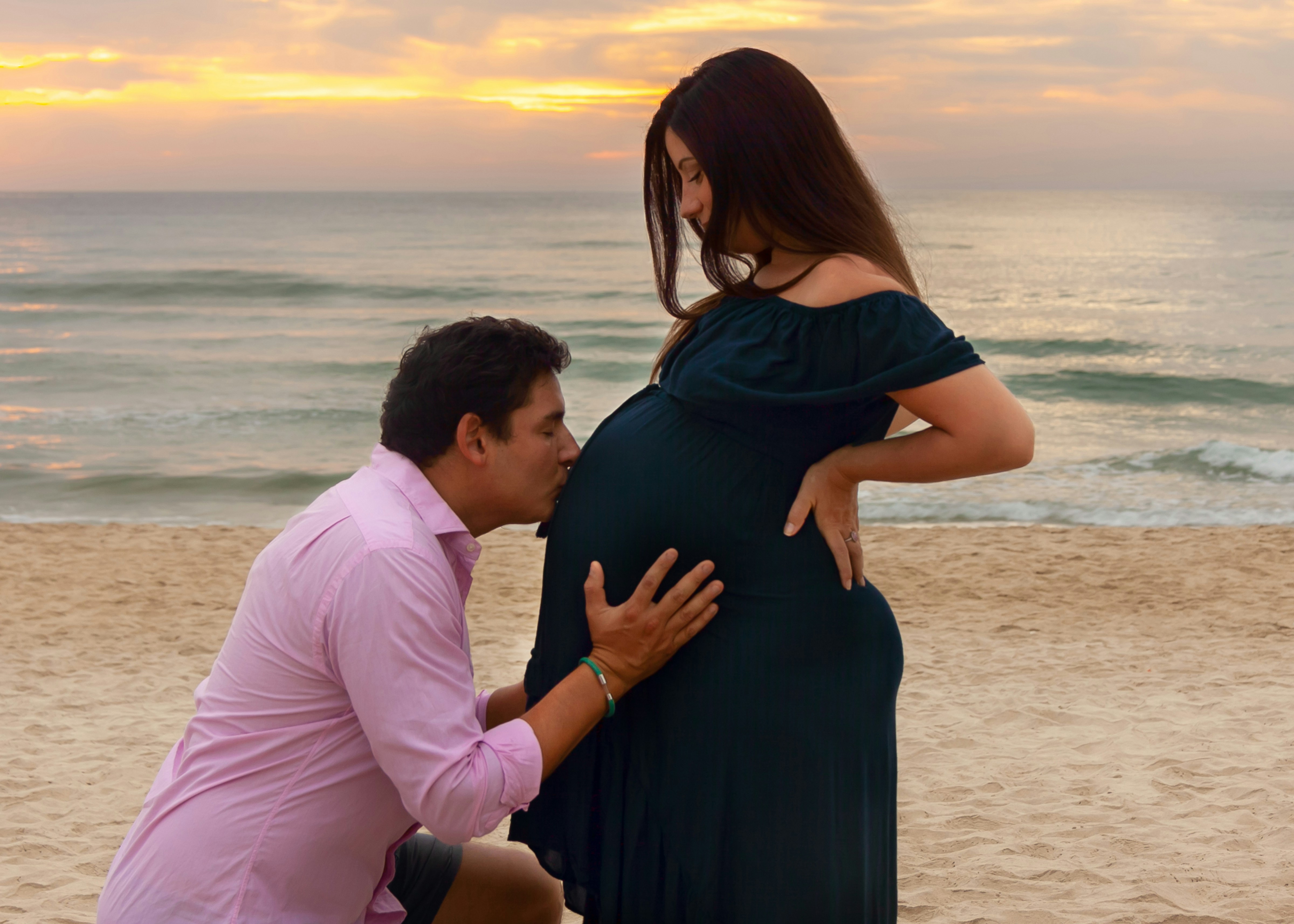 A man kneeling down next to a pregnant woman on a beach