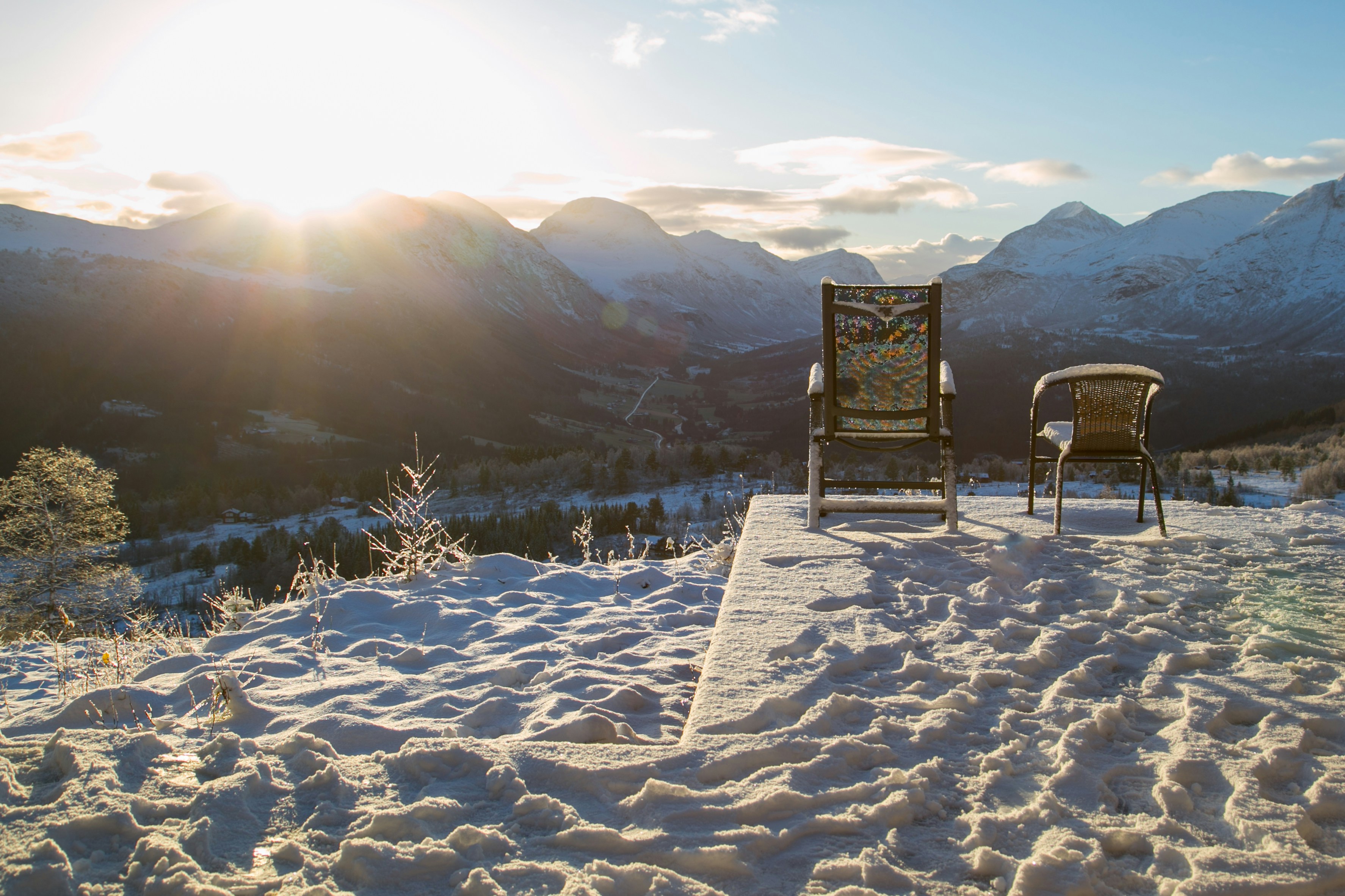 Two lawn chairs sitting on top of a snow covered slope