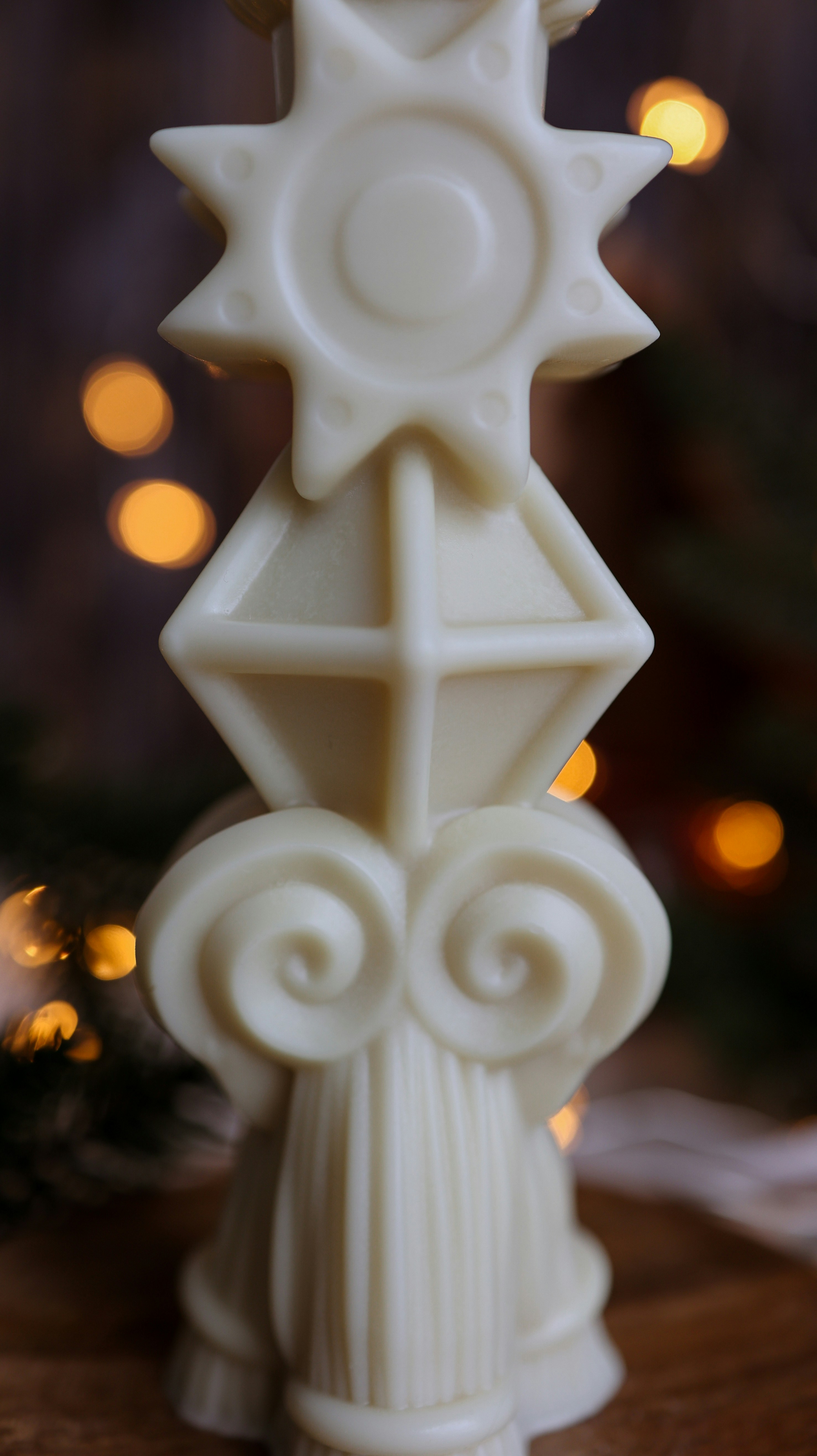 A close up of a candle on a table near a christmas tree