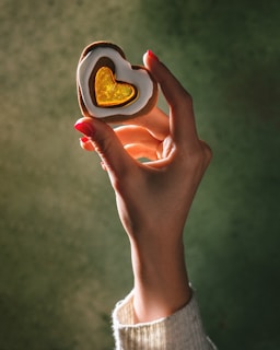 A person holding a heart shaped cookie in their hand