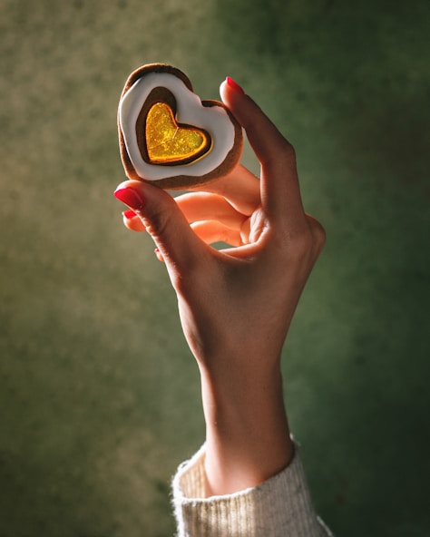 A person holding a heart shaped cookie in their hand
