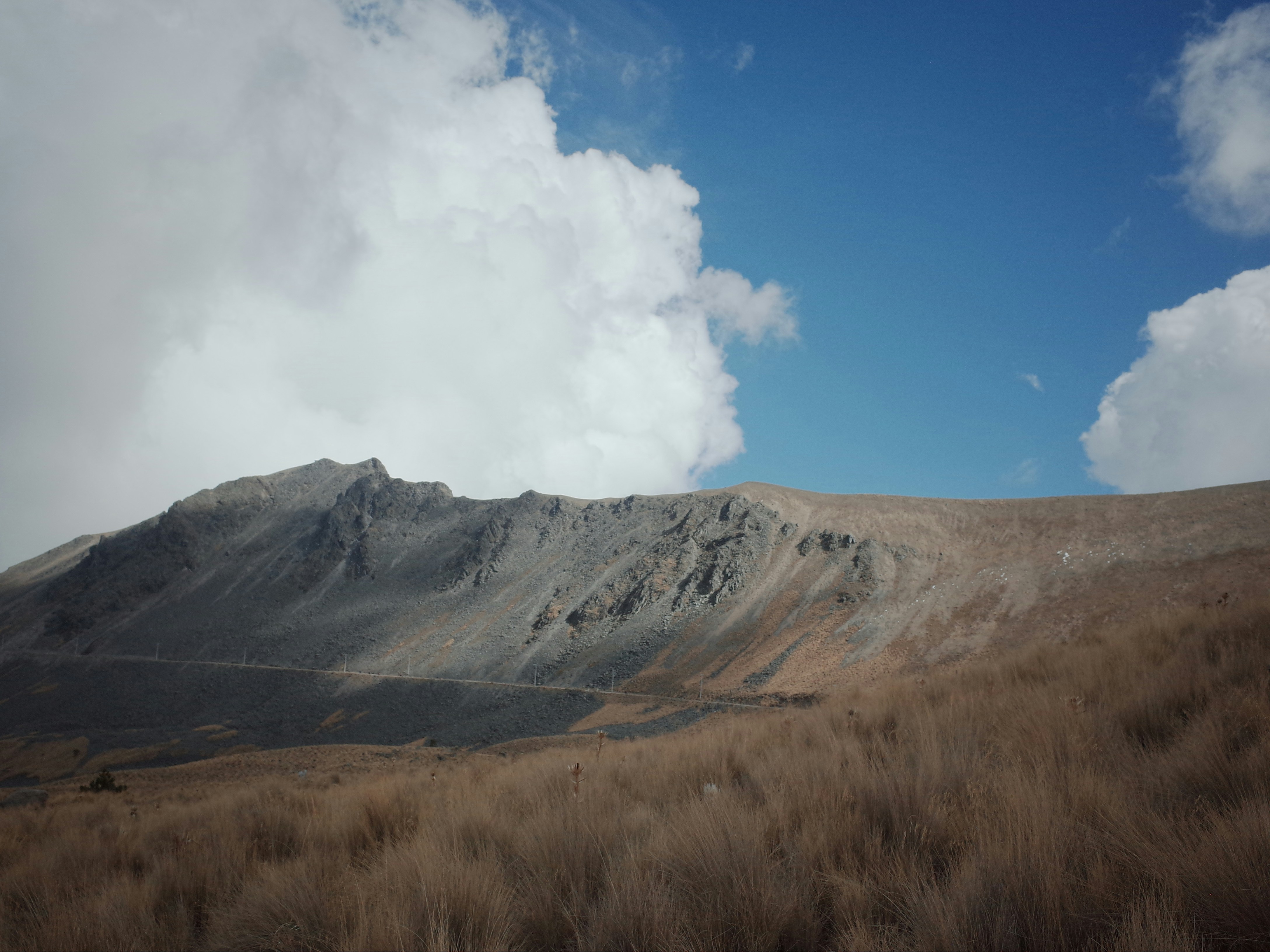 A hill with a grassy field below and clouds in the sky