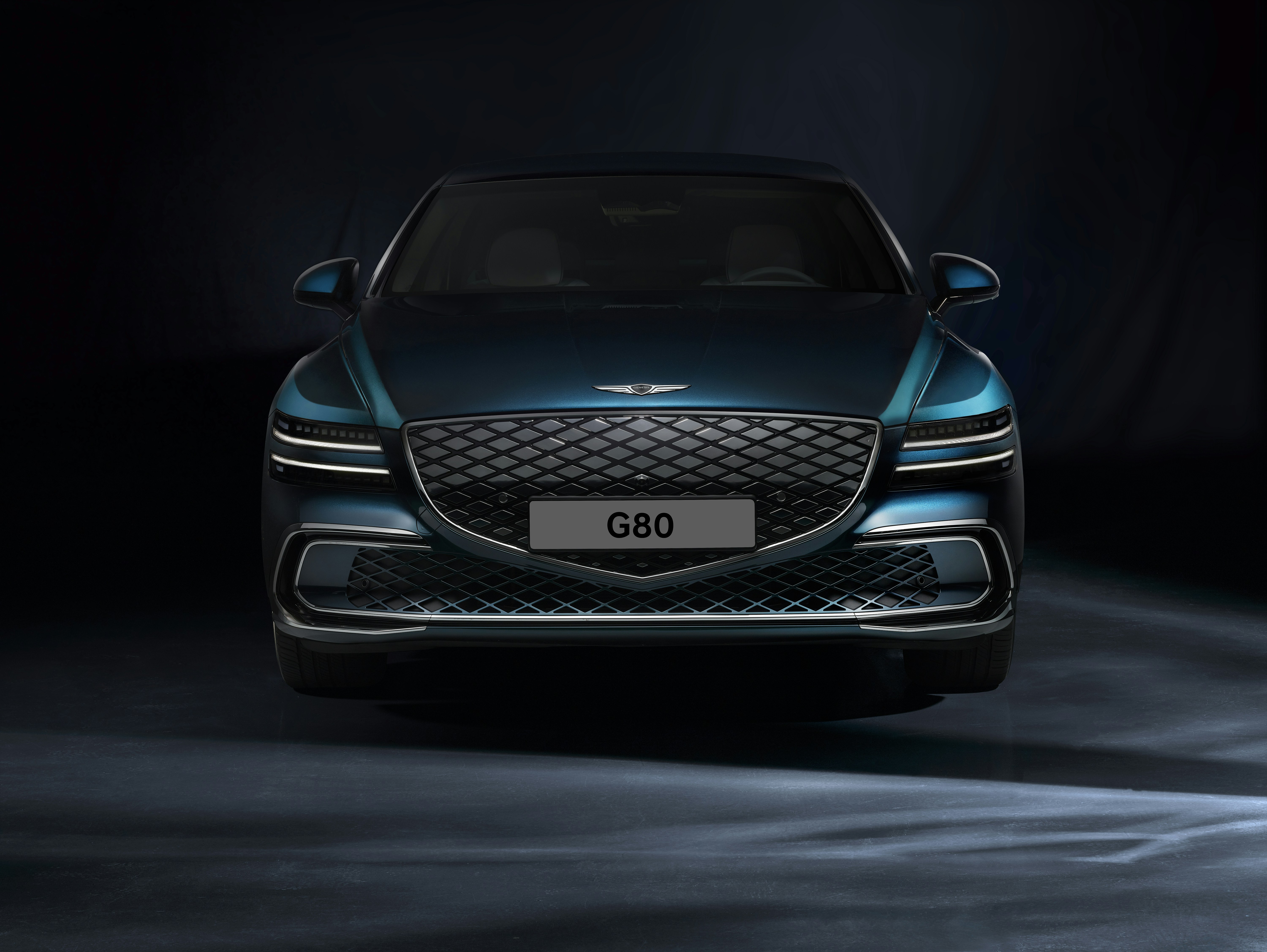 Dark navy Genesis G80 luxury sedan parked at a hotel entrance, bold crest grille and sculpted lines with premium Korean craftsmanship
