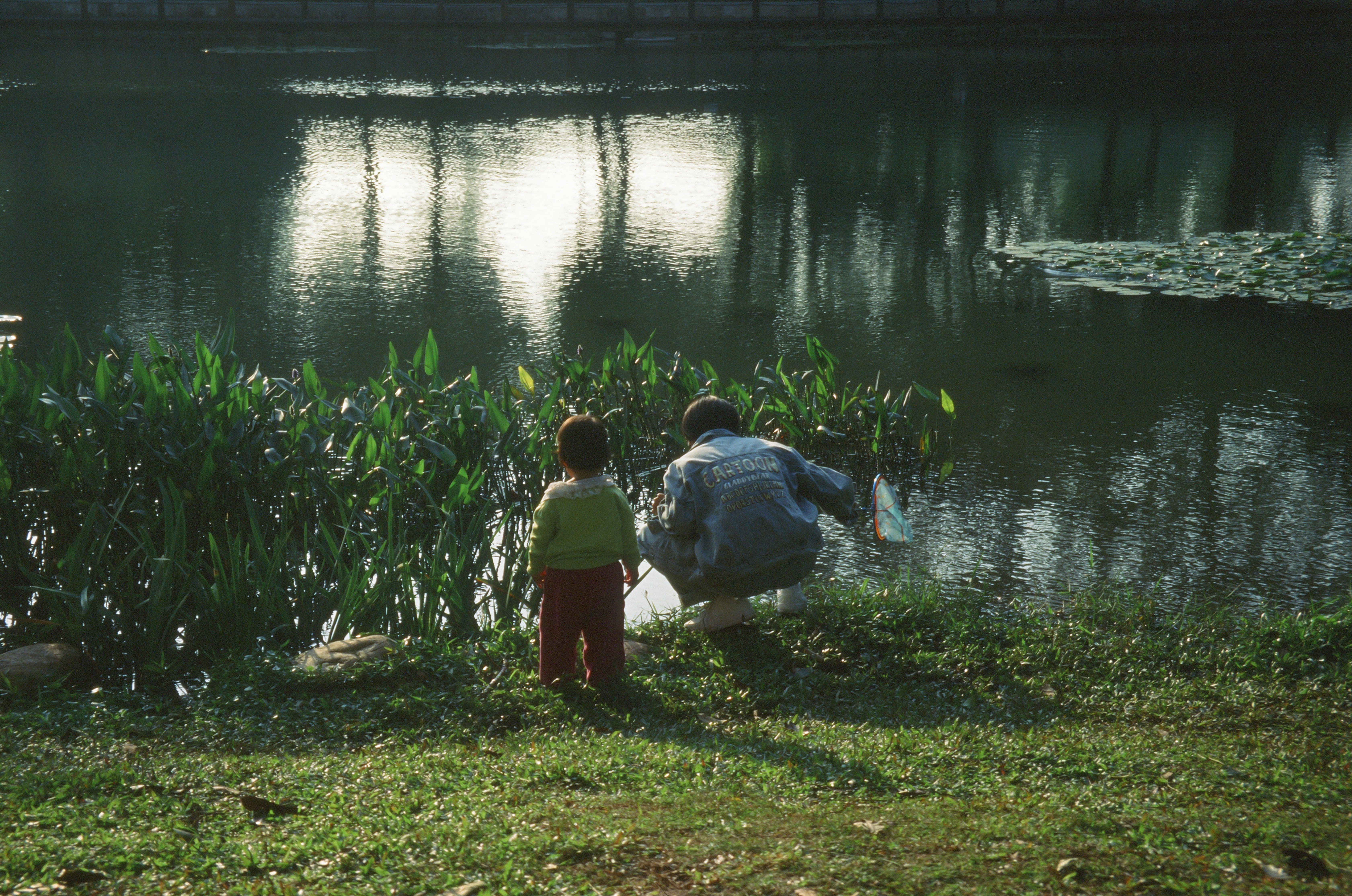 一位父親在平靜的湖邊教他的小兒子如何釣魚。