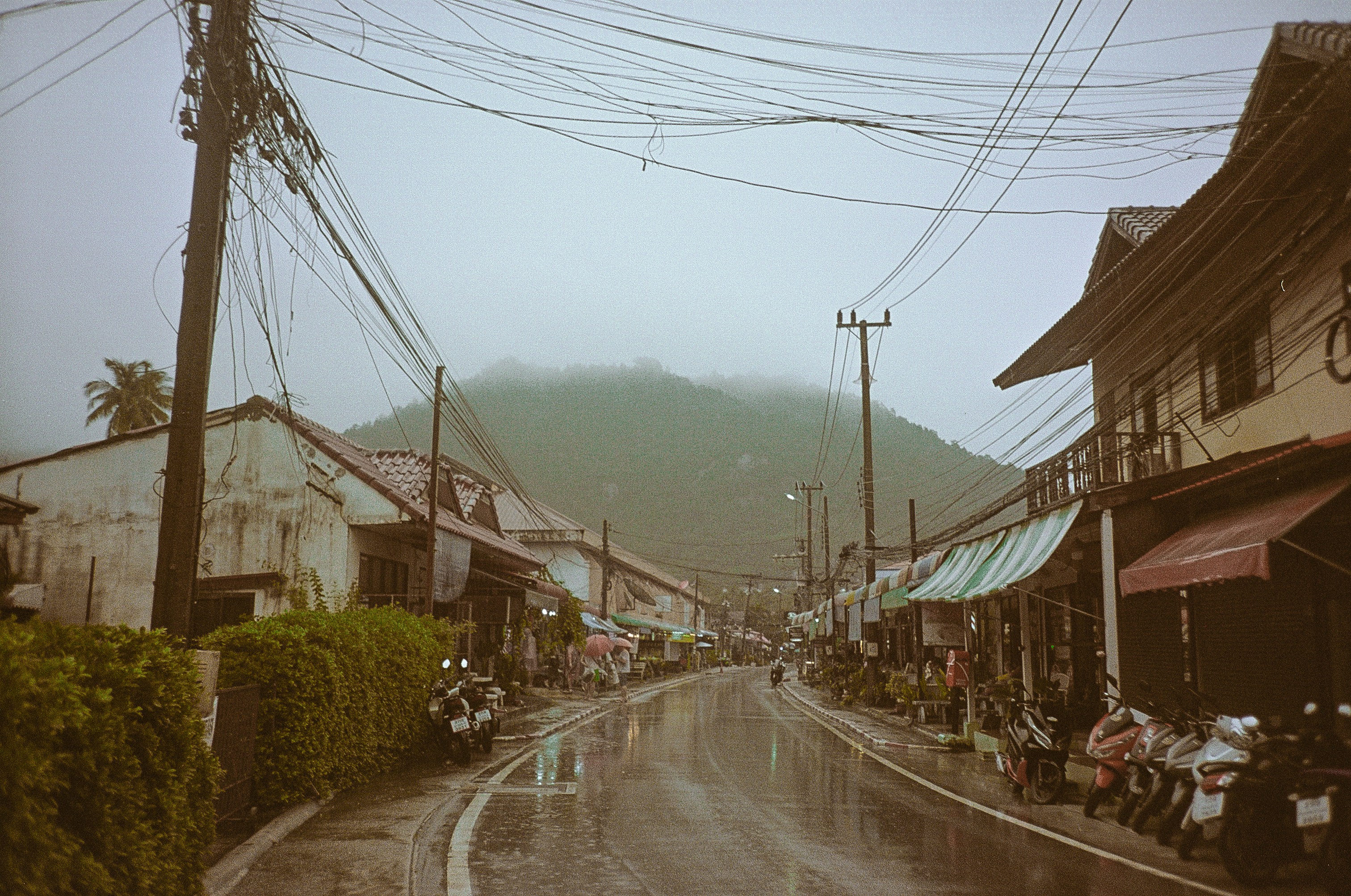A wet street with a bunch of motor bikes parked on the side of it