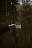 A person holding a cup of coffee in a forest