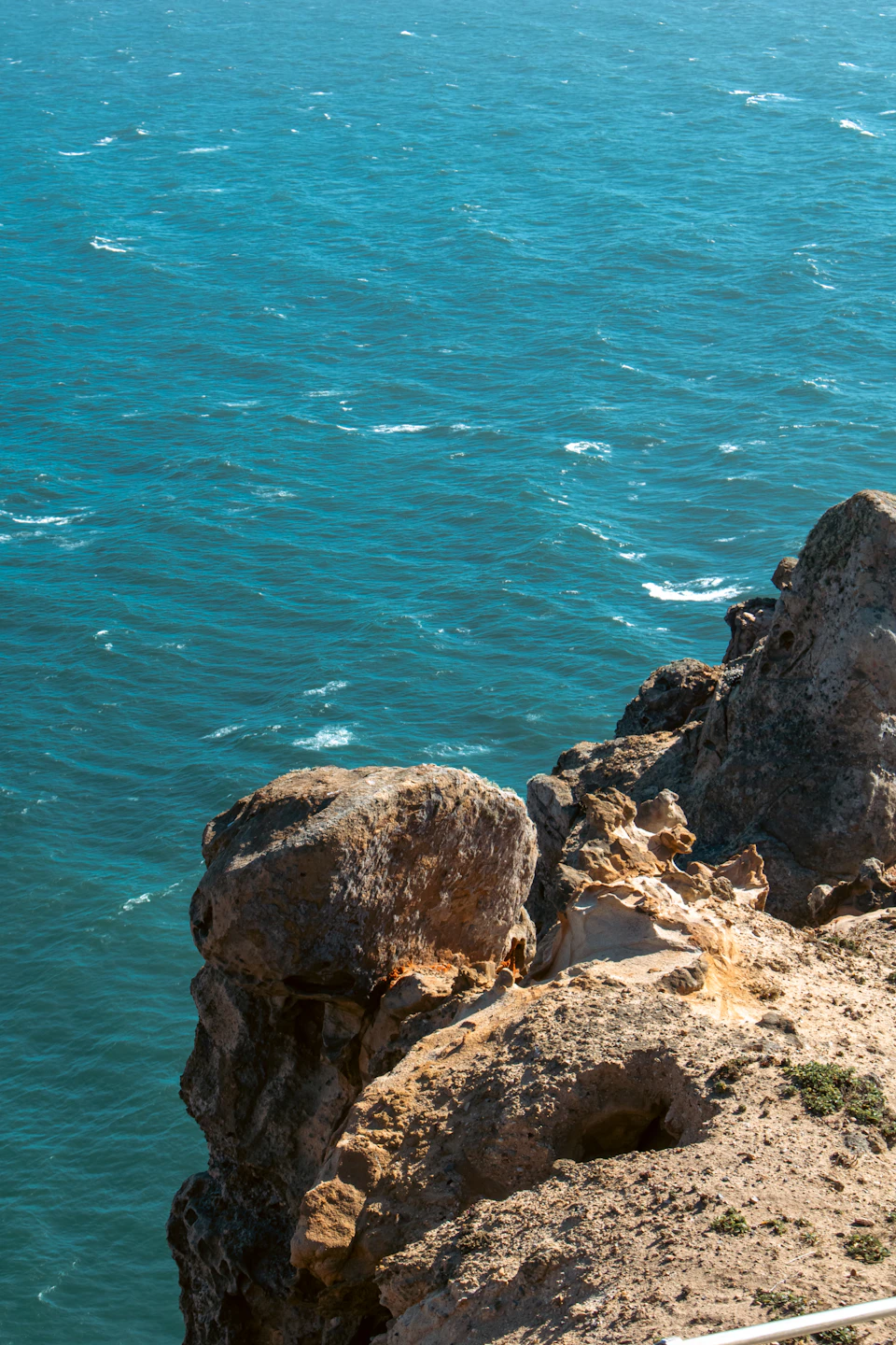 Rocky cliff overlooking ocean with deep blue water creating striking contrast against the sky