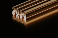 Four lengths of extrusion stock standing on end against black, each catching a warm rim of light
