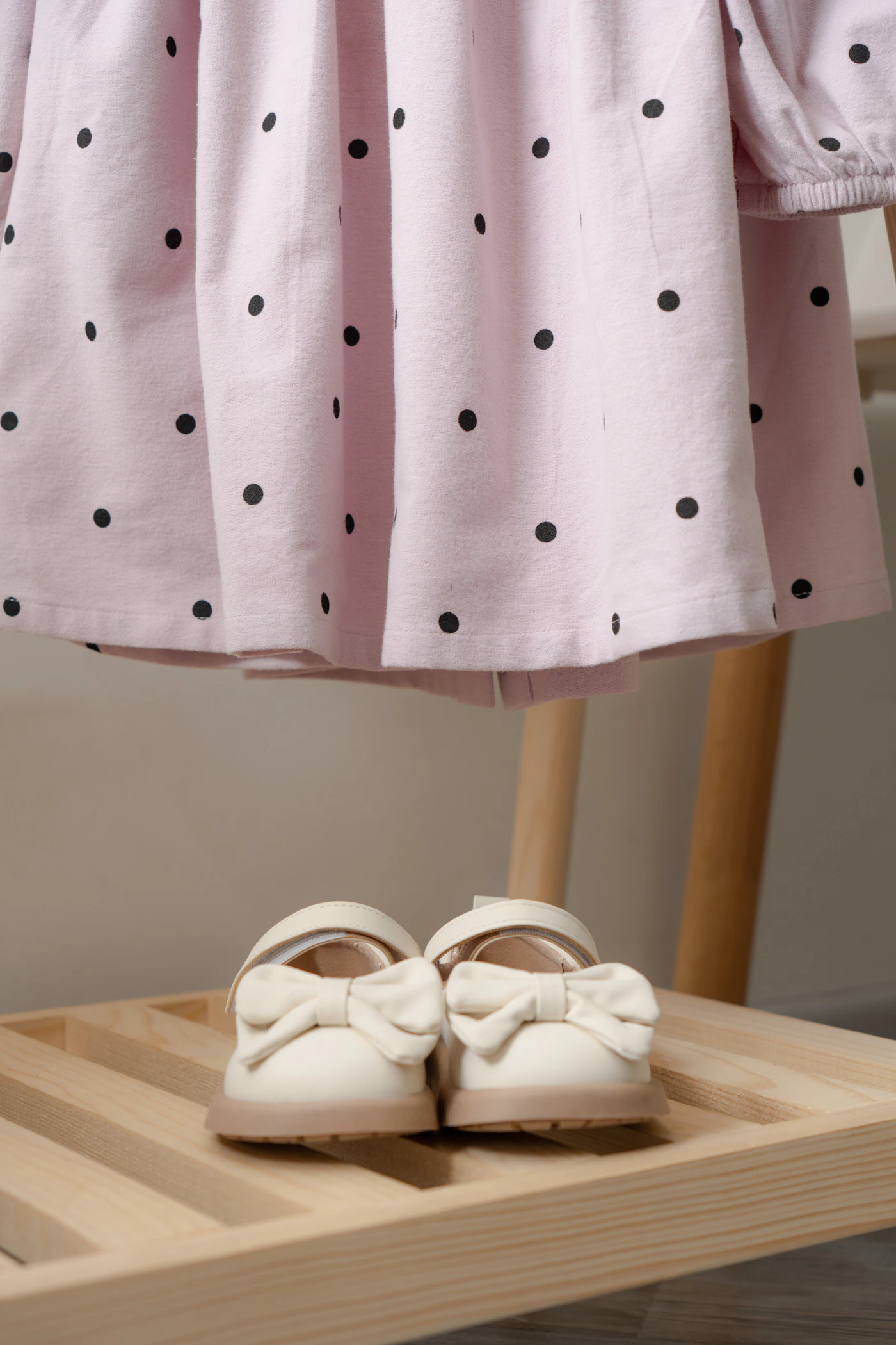 Tiny cream baby shoes with bows styled beside a soft pink dress