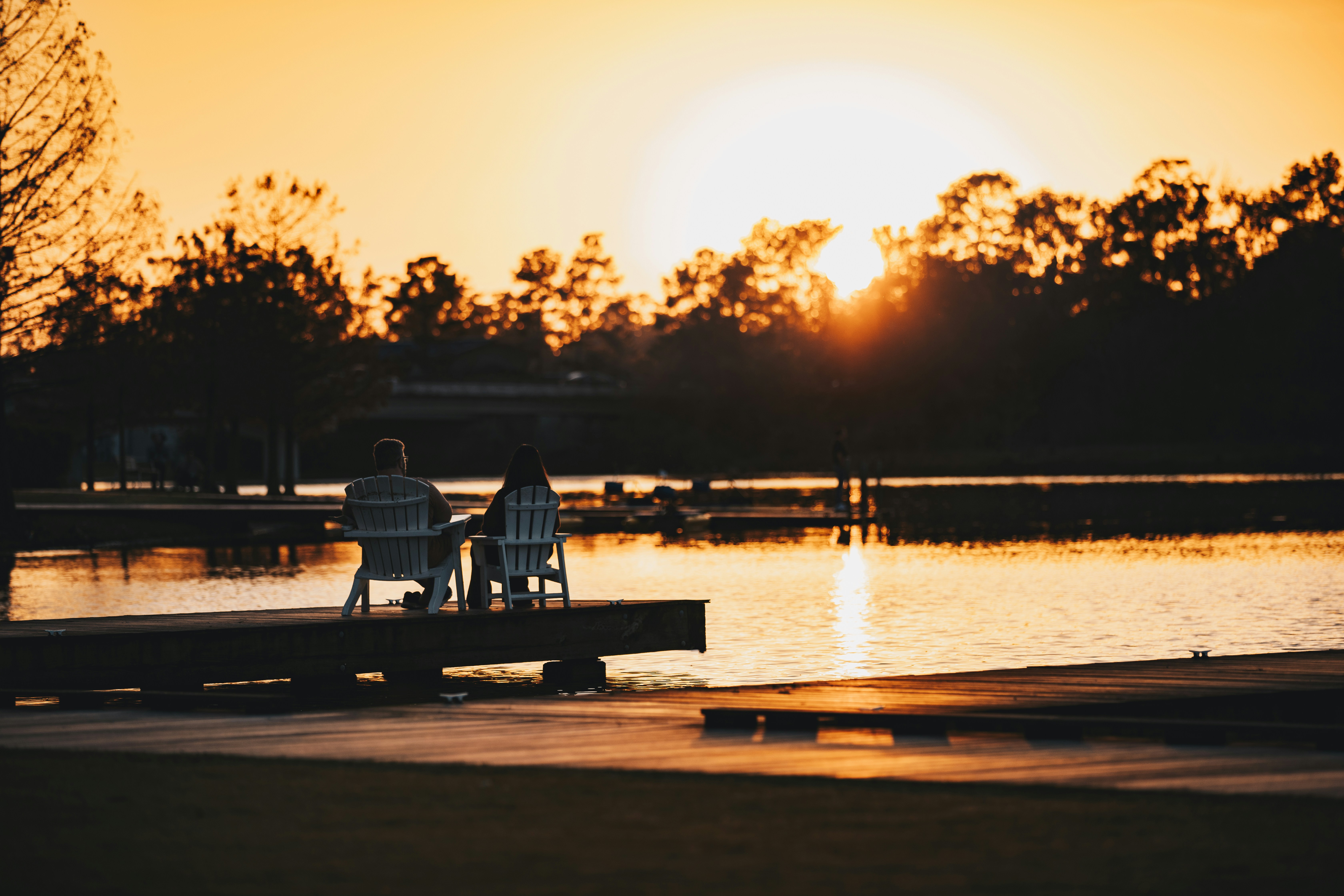 A quiet riverside park at sunset, two old friends sitting on a weathered wooden bench, their reflections shimmering in the golden water.