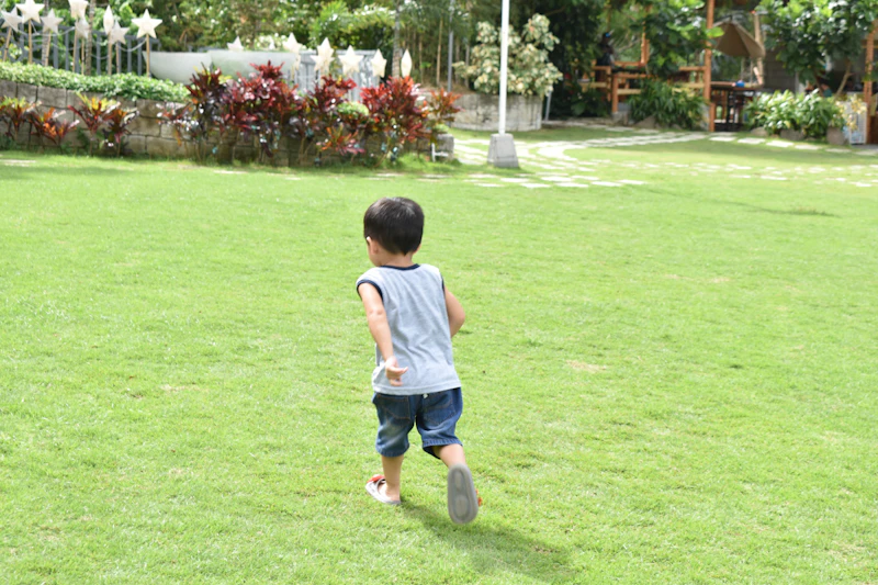 A young boy running across a sunny green lawn