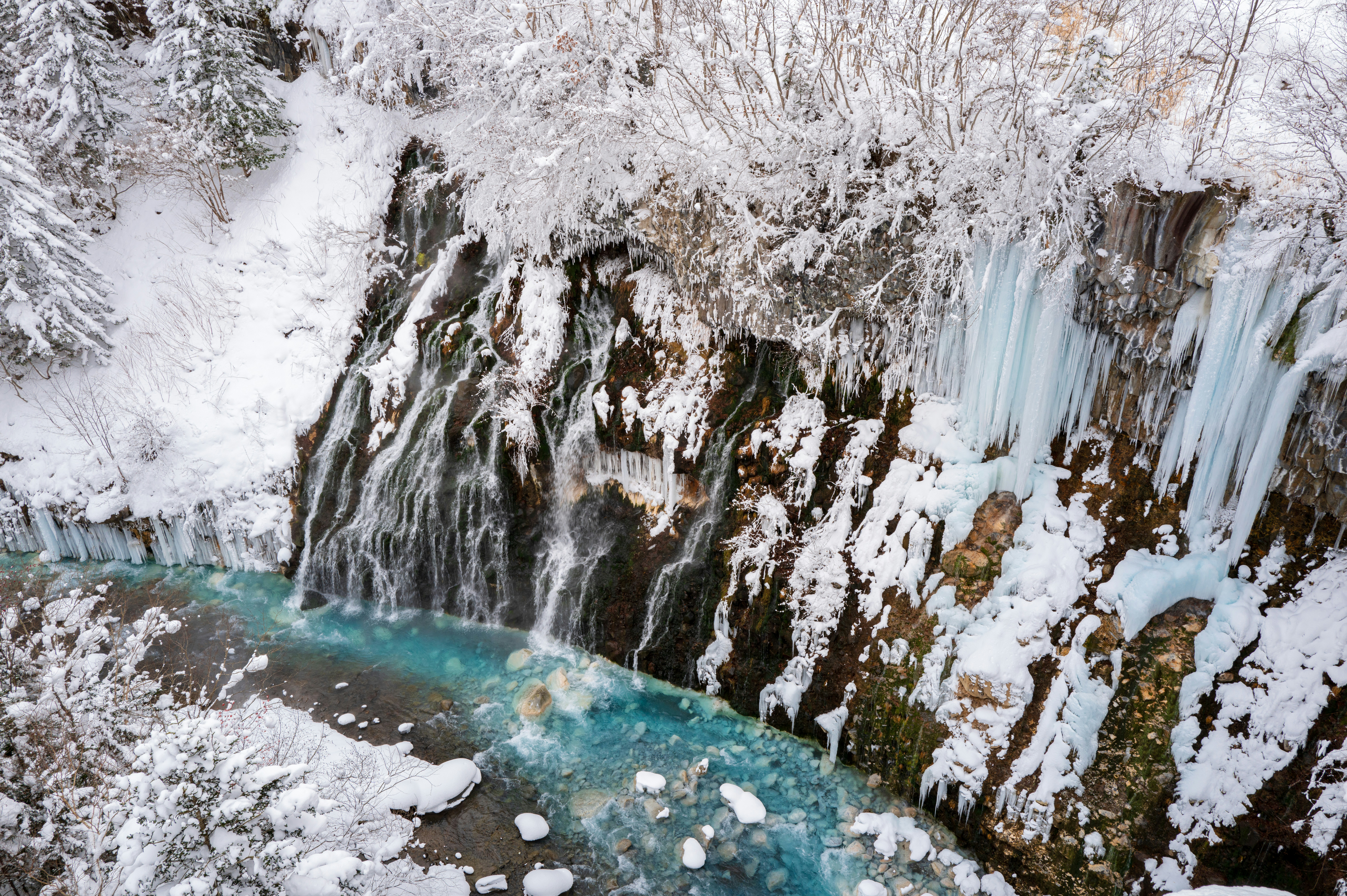An aerial view of a frozen waterfall in the woods