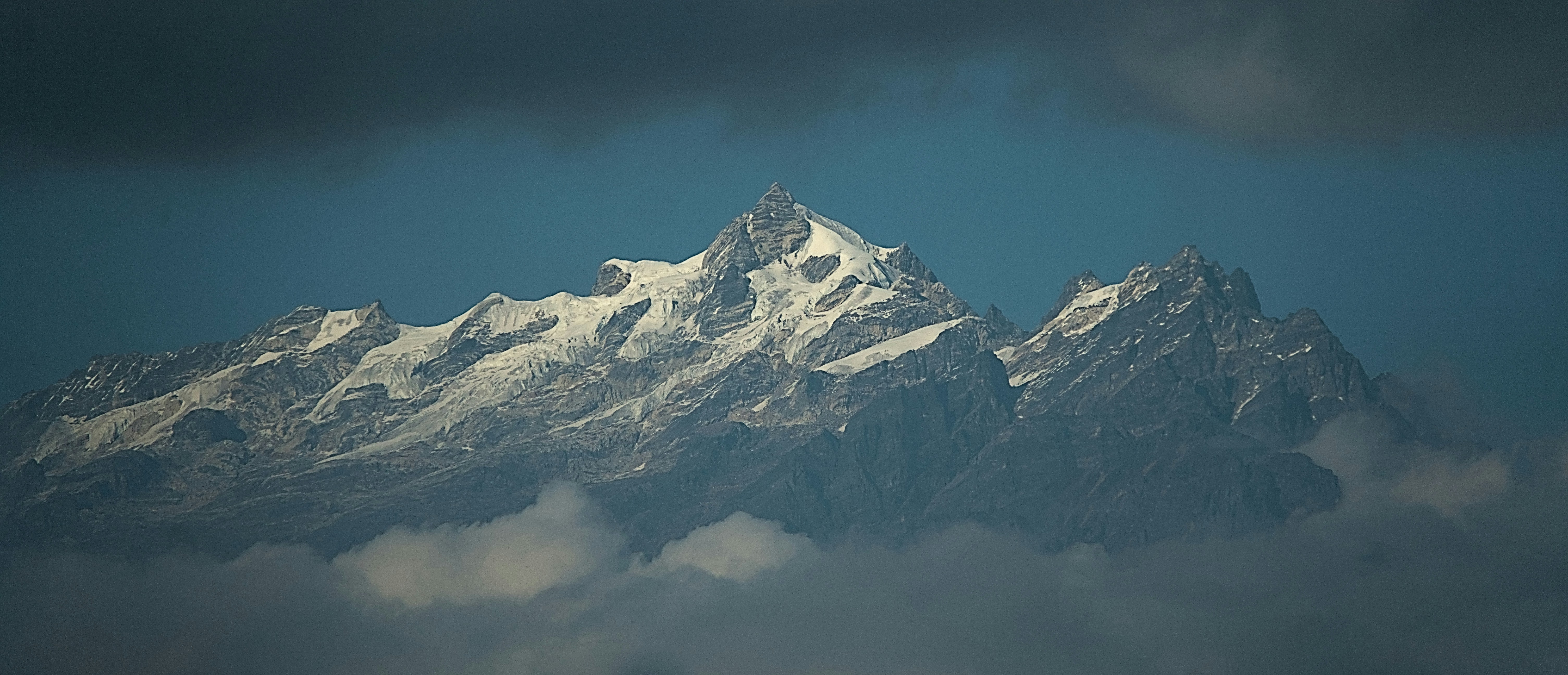 A snow covered mountain is seen through the clouds