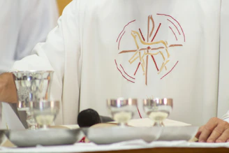A priest standing in front of a table with silver cups
