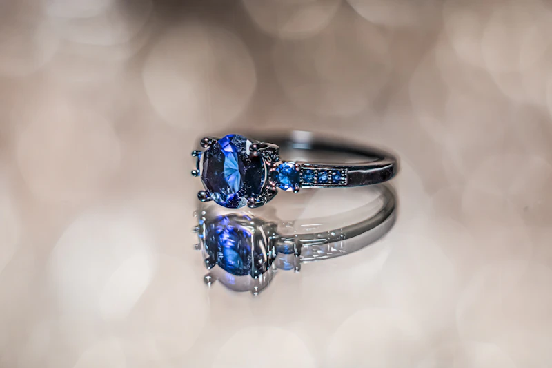 Oval blue sapphire ring with diamond shoulders reflected on a glossy surface