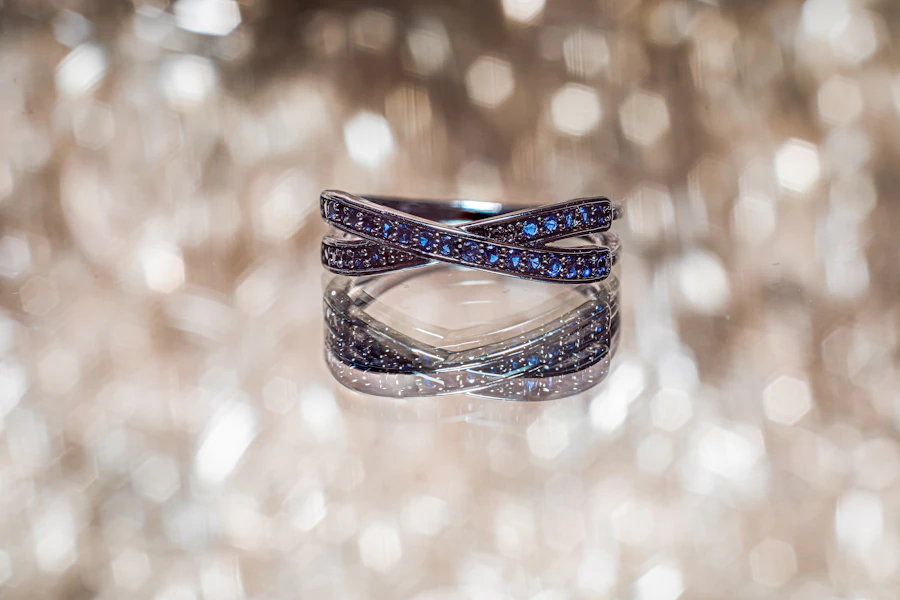 A ring of two crossed bands set with tiny blue stones, against a soft glitter of light