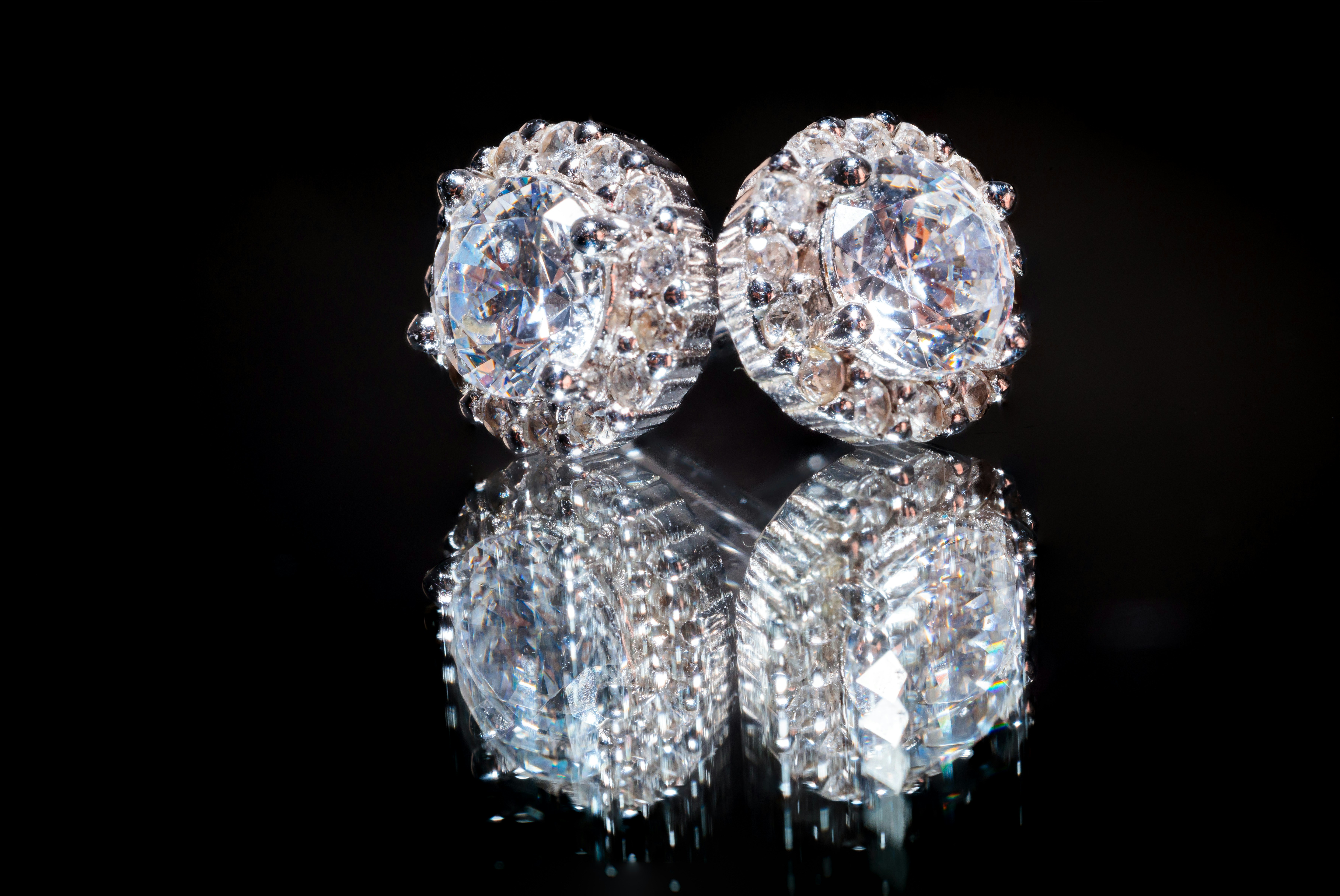 A pair of diamond earrings on a reflective surface