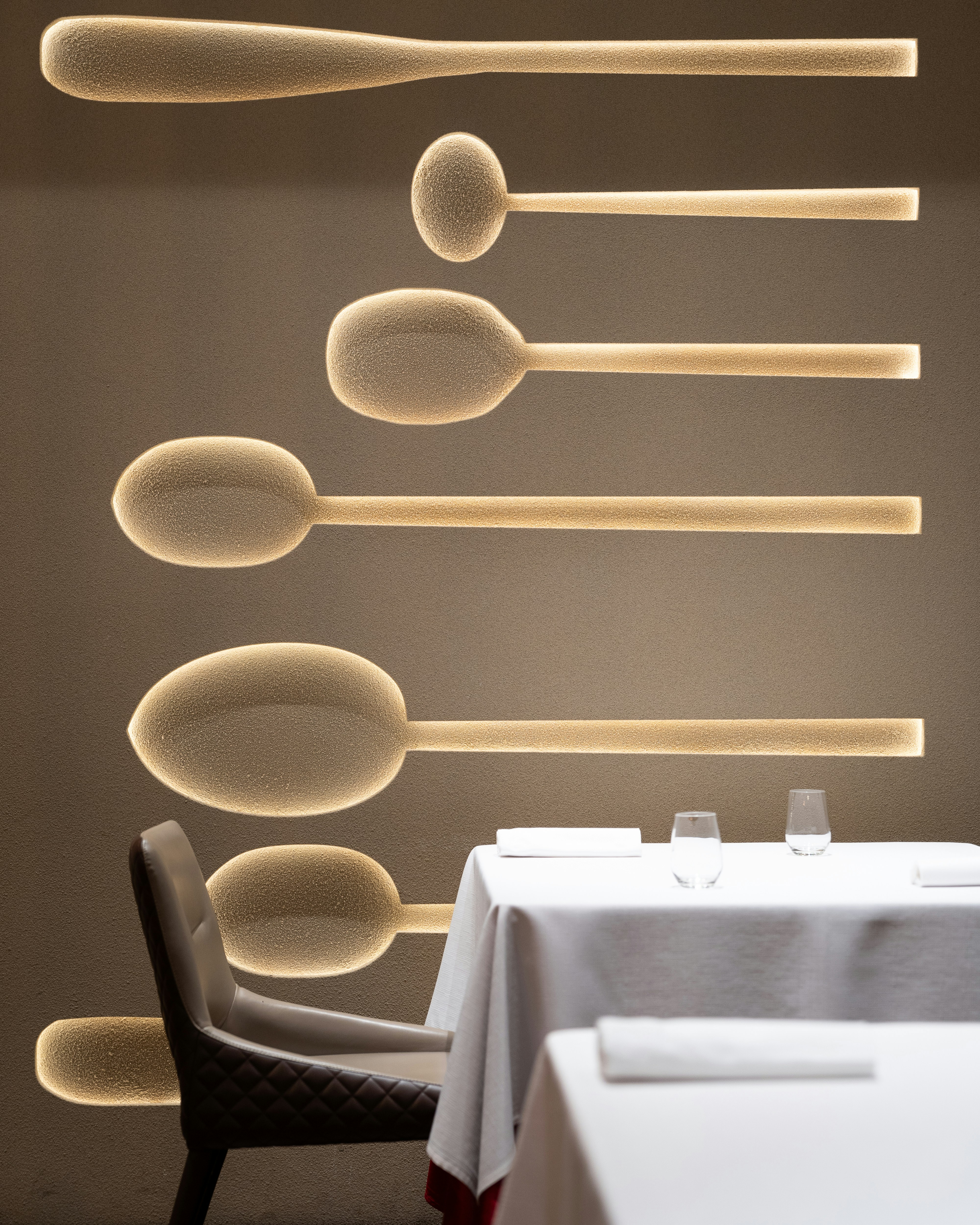 Dining tables set with white tablecloths near spoon-shaped wall lights.