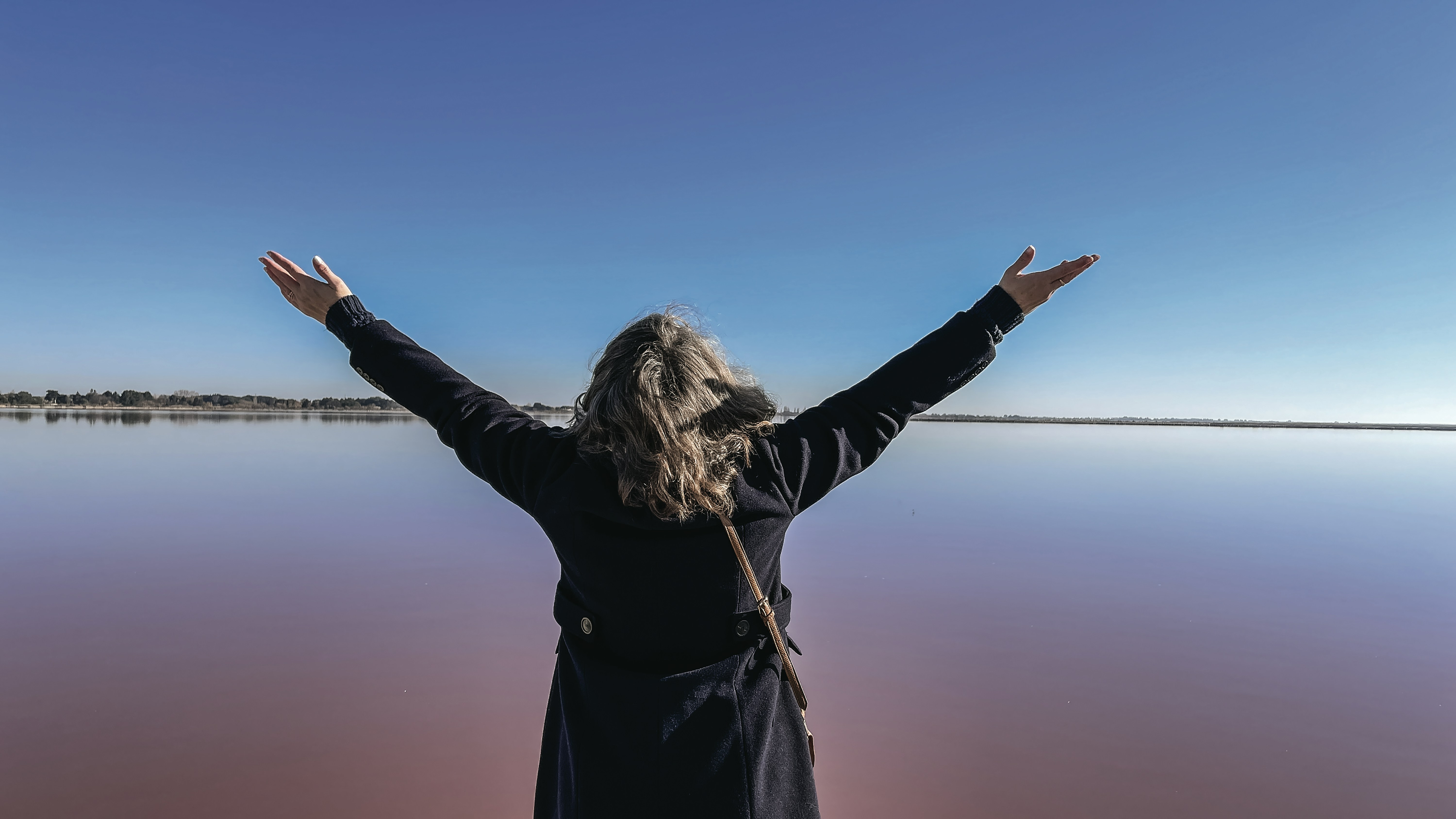A woman with her arms outstretched in front of a body of water