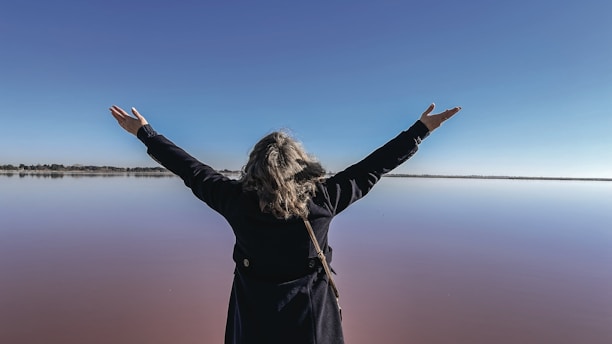 A woman with her arms outstretched in front of a body of water