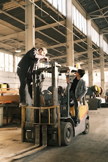 A man standing on top of a forklift in a warehouse
